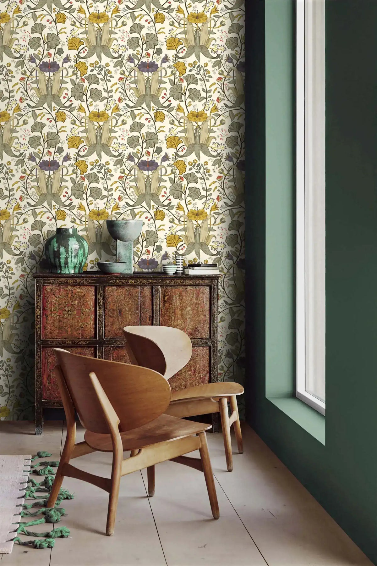 Vintage yellow floral wallpaper beside a sage green wall, with a carved cabinet, green vases, and wood lounge chair