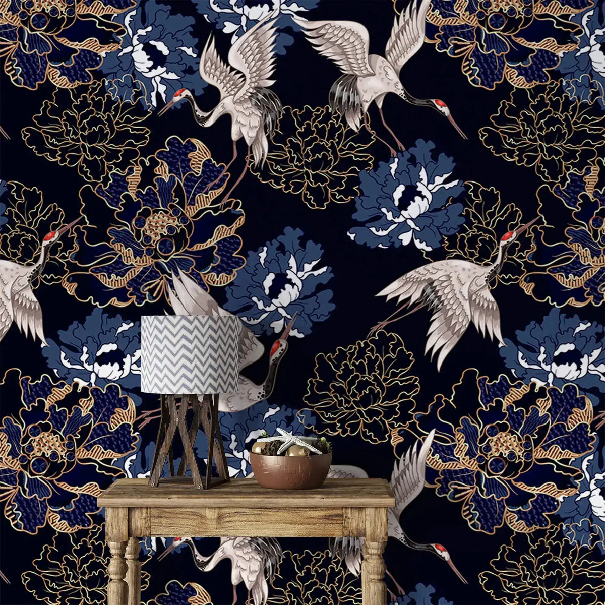 Golden crane flight wallpaper, white cranes among blue and gold peonies on navy, styled with a lamp