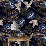 Golden crane flight wallpaper, white cranes among blue and gold peonies on navy, styled with a lamp