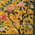Area rug with a vibrant golden background featuring a hand-tufted wool design. The rug displays an intricate pattern of blooming pink flowers and lush green leaves with a colorful bird perched on a branch, perfect for adding a contemporary touch to large living room spaces.