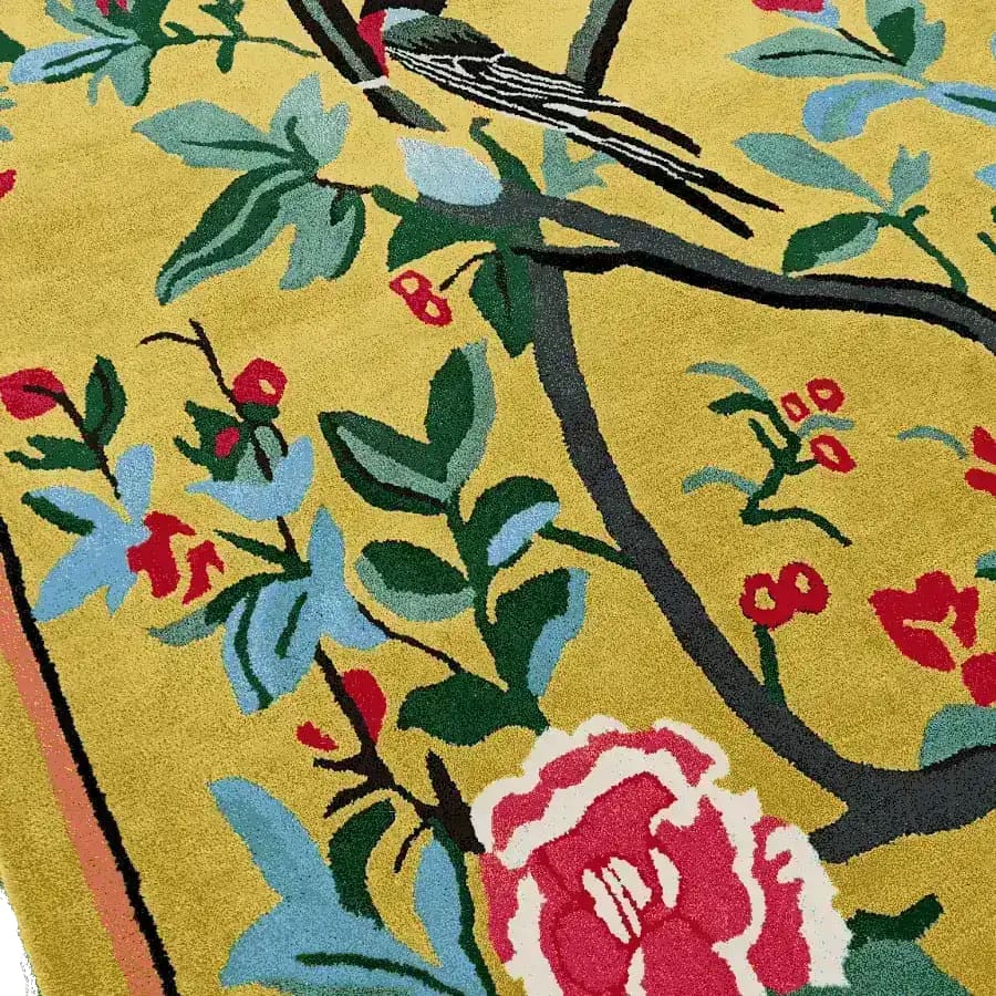 Close-up view of the Golden Garden Hand Tufted Rug showcasing a vibrant floral design with a bird perched on a branch. This wool area rug, perfect for dining rooms and living rooms, features rich colors like red, green, and blue against a golden background, making it an ideal choice for adding a touch of elegance to any space.