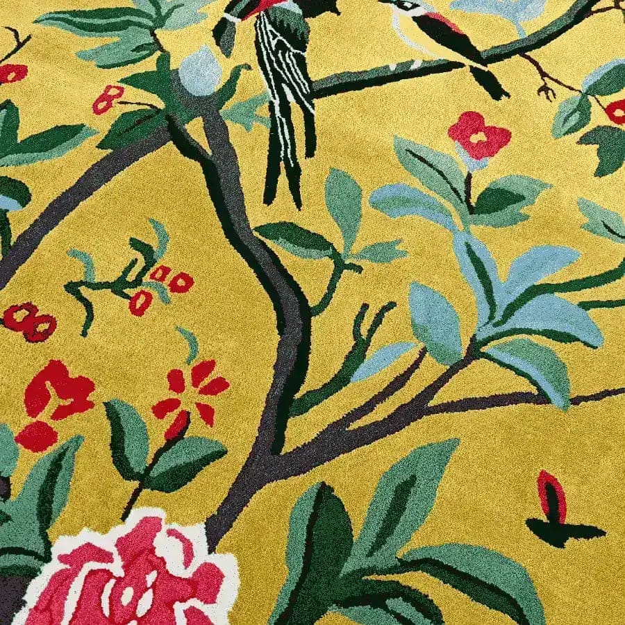 Golden Garden Hand Tufted Area Rug with a vibrant floral design featuring birds perched on branches, ideal for dining room or living room decor. This wool rug showcases a rich tapestry of red, blue, and green colors on a warm golden background, perfect as a dining room area rug or a striking floral rug centerpiece.