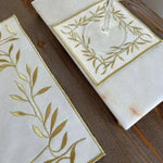 Golden Leaf Elegance placemat and coaster side view with gold embroidered olive sprigs and wine glass on rustic wood