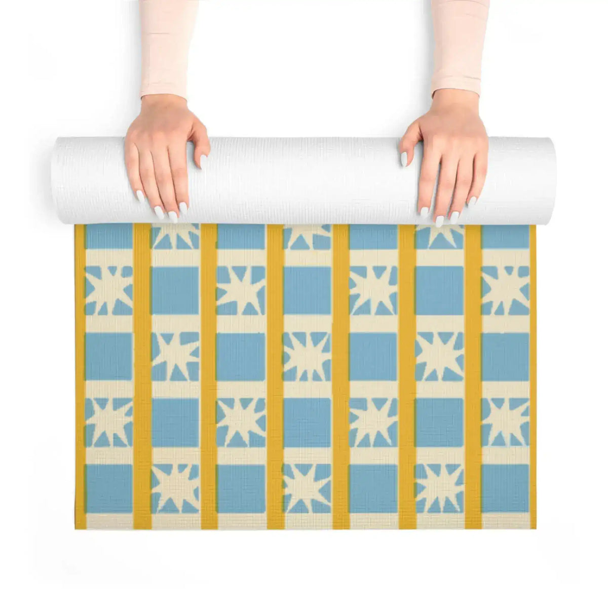 Hands unrolling Golden Solstice yoga mat revealing blue squares, cream stars and gold stripes