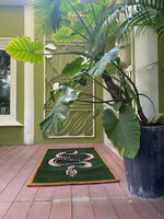 The Green and Black Snake Hand Tufted Wool Area Rug is elegantly displayed on a wooden patio surrounded by lush greenery. This vintage rug, perfect for a dining room setting, features a striking snake design on a deep green background, making it an ideal choice for a dining table rug or living room rugs 8x10. The wool rug's intricate design adds a touch of sophistication to any living room decor.