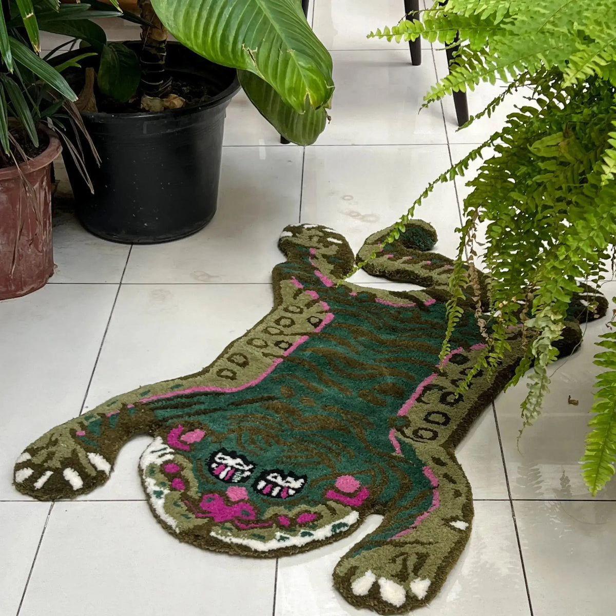 A vibrant Green Asian Tiger Wool Rug elegantly displayed on a tiled floor, surrounded by lush greenery. This vintage area rug features an abstract tiger design with rich greens and pink accents, perfect for adding a touch of exotic charm to a dining room, office, or formal dining room. Ideal as a dining room carpet, this wool rug combines artistry with functionality.