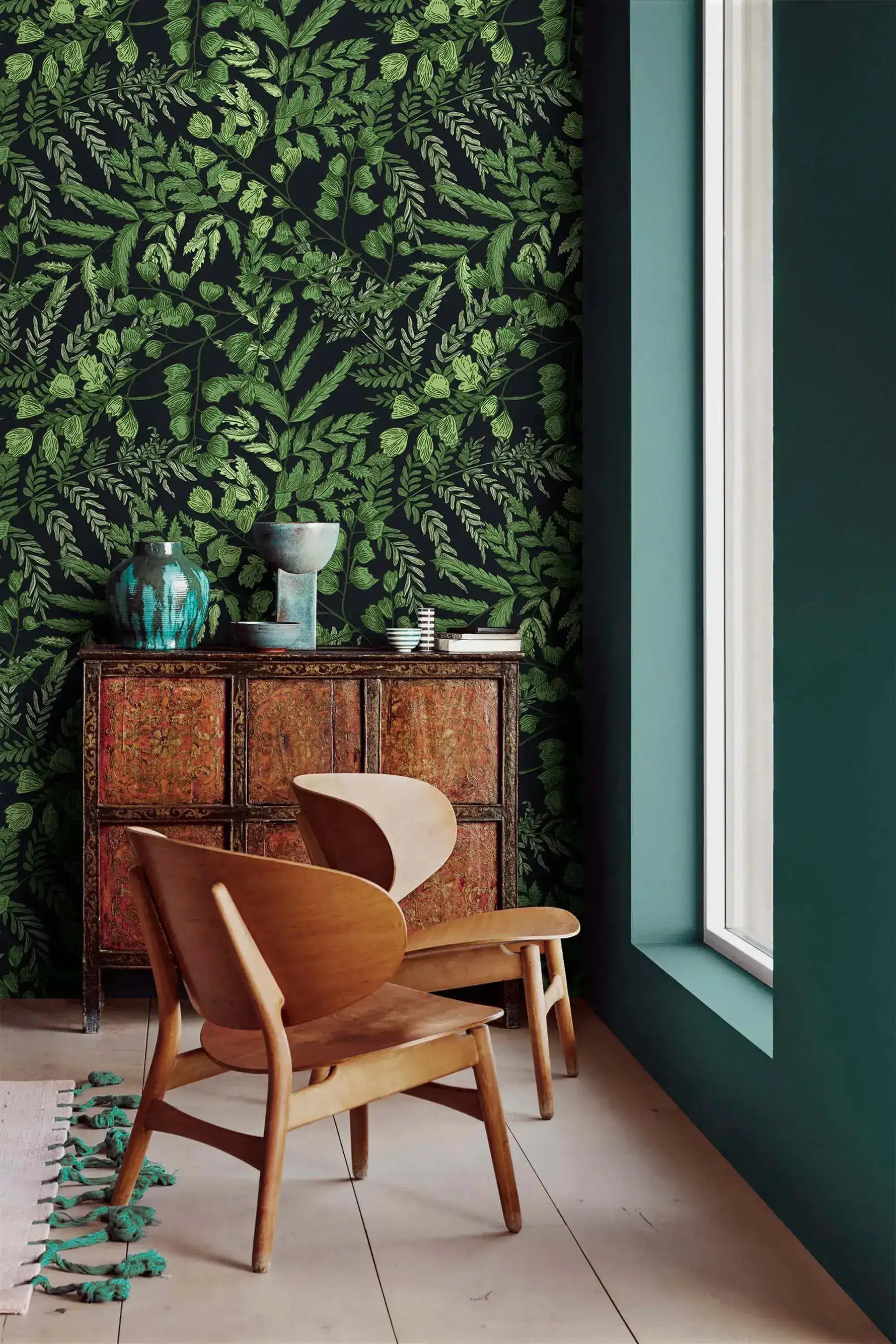 Green fern foliage wallpaper next to a teal wall with antique cabinet and curved wood chairs