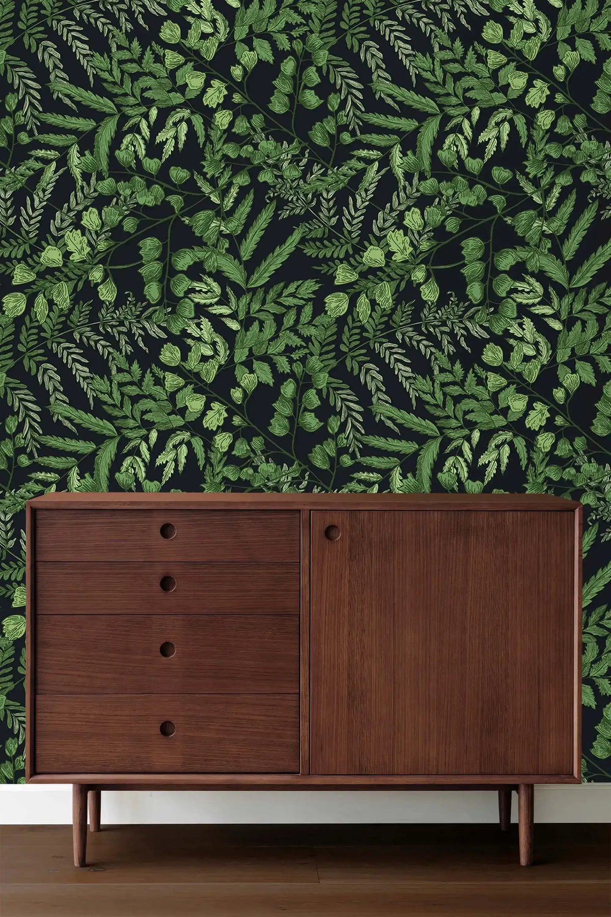 Green fern foliage wallpaper on dark ground behind a mid-century walnut sideboard