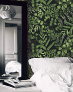 Green fern foliage wallpaper on dark ground beside a tall mirror and a bed with white linens