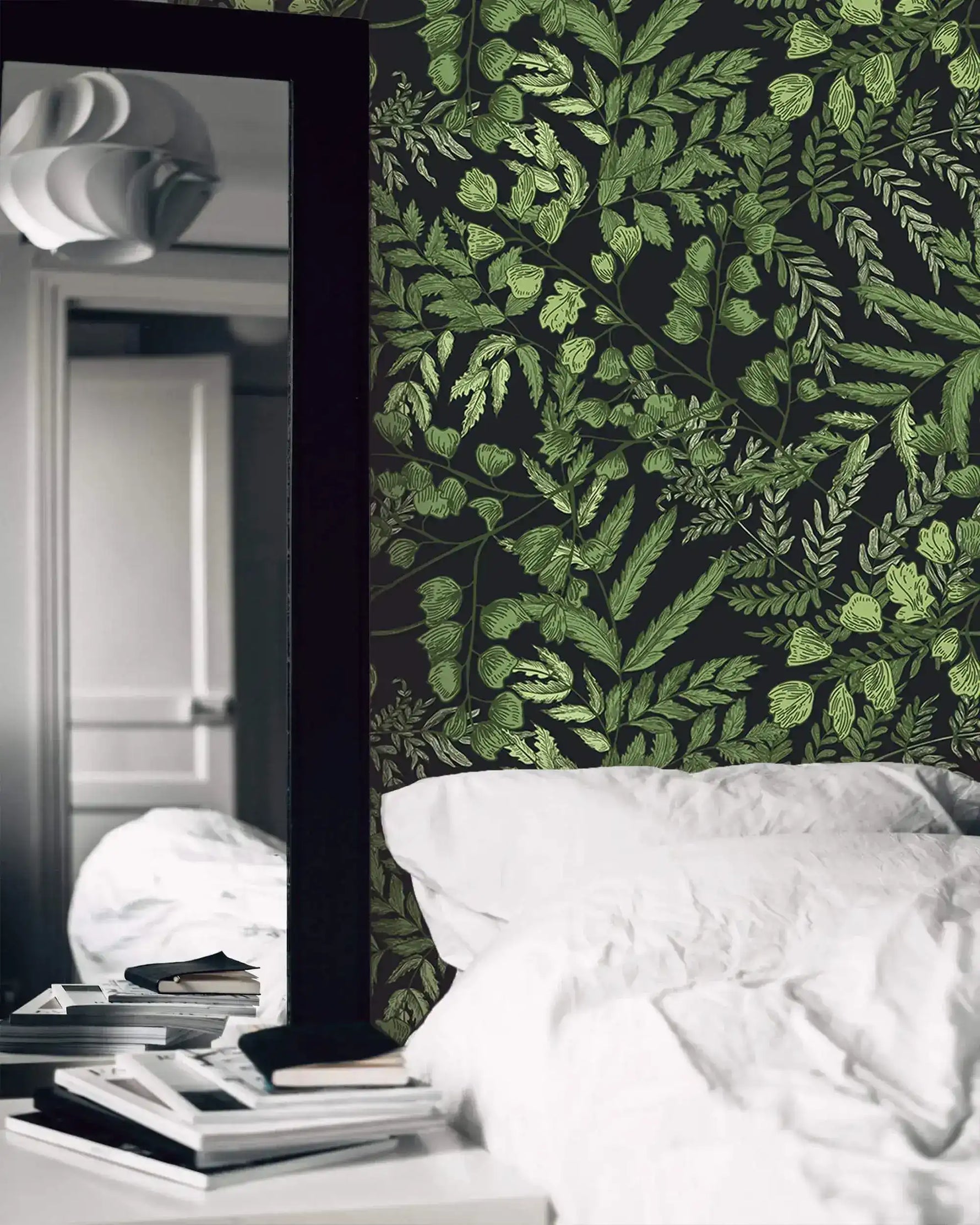 Green fern foliage wallpaper on dark ground beside a tall mirror and a bed with white linens