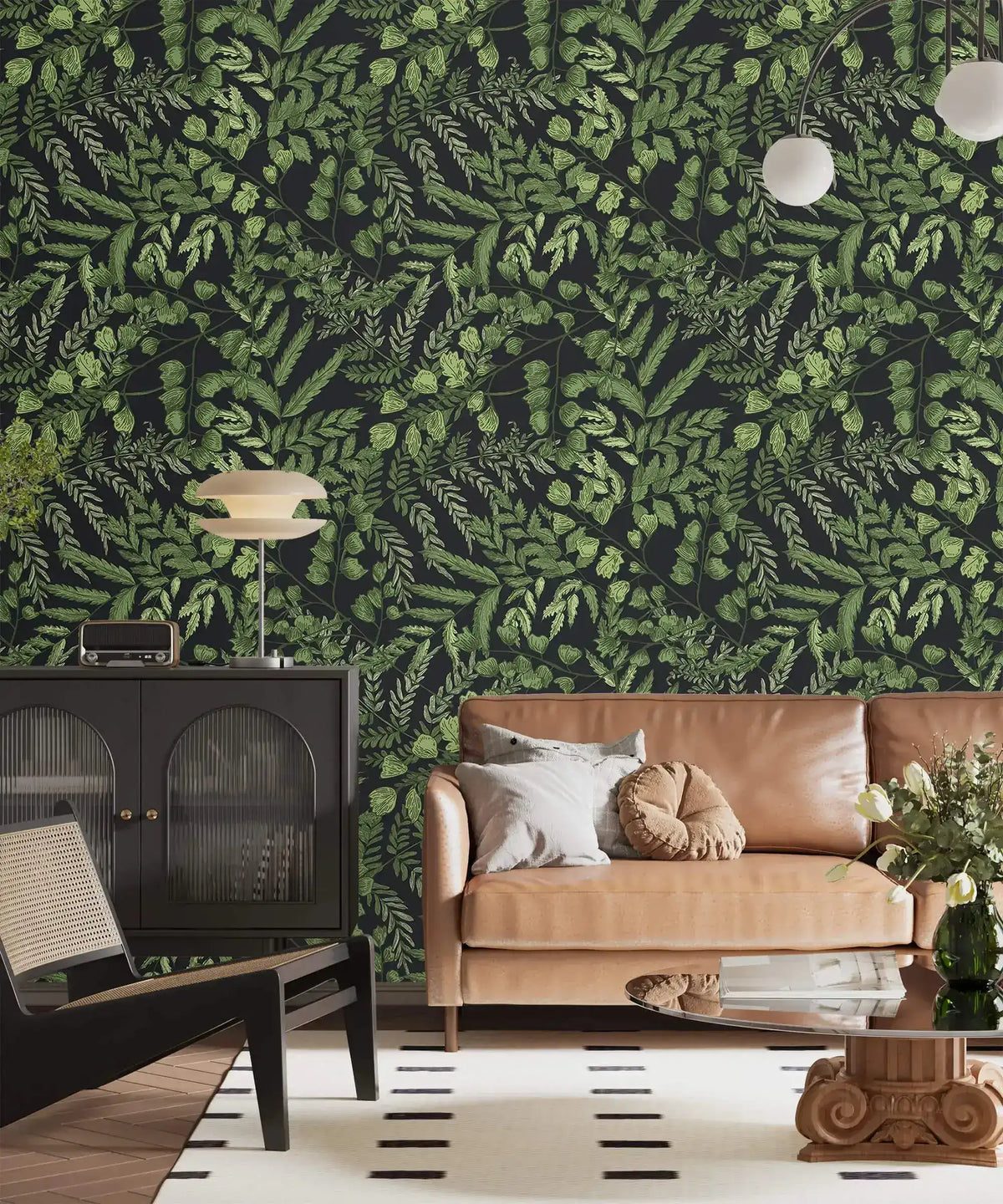Green fern foliage wallpaper on dark ground in a lounge with tan sofa, black cabinet and globe lamp
