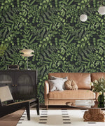 Green fern foliage wallpaper on dark ground in a lounge with tan sofa, black cabinet and globe lamp