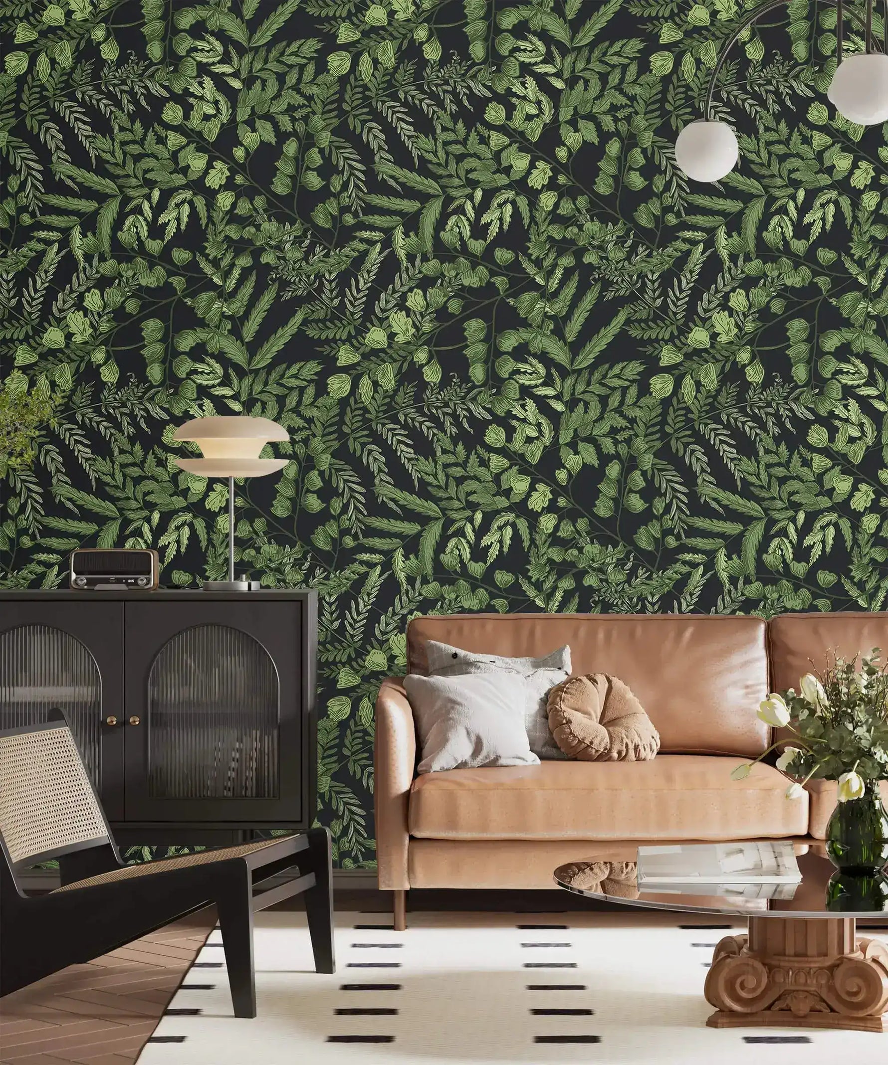 Green fern foliage wallpaper on dark ground in a lounge with tan sofa, black cabinet and globe lamp