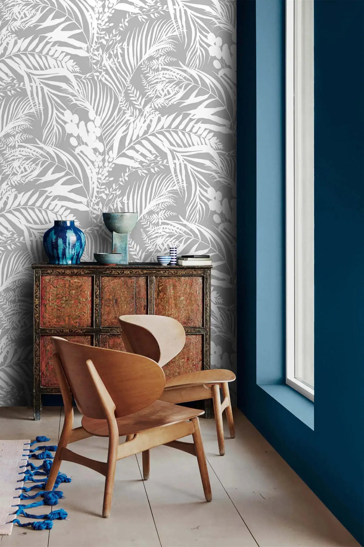 Grey Tropical Foliage Wallpaper above an ornate red cabinet and pair of wood chairs