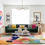 Modern living room with a green sofa, colorful rug, and abstract art.