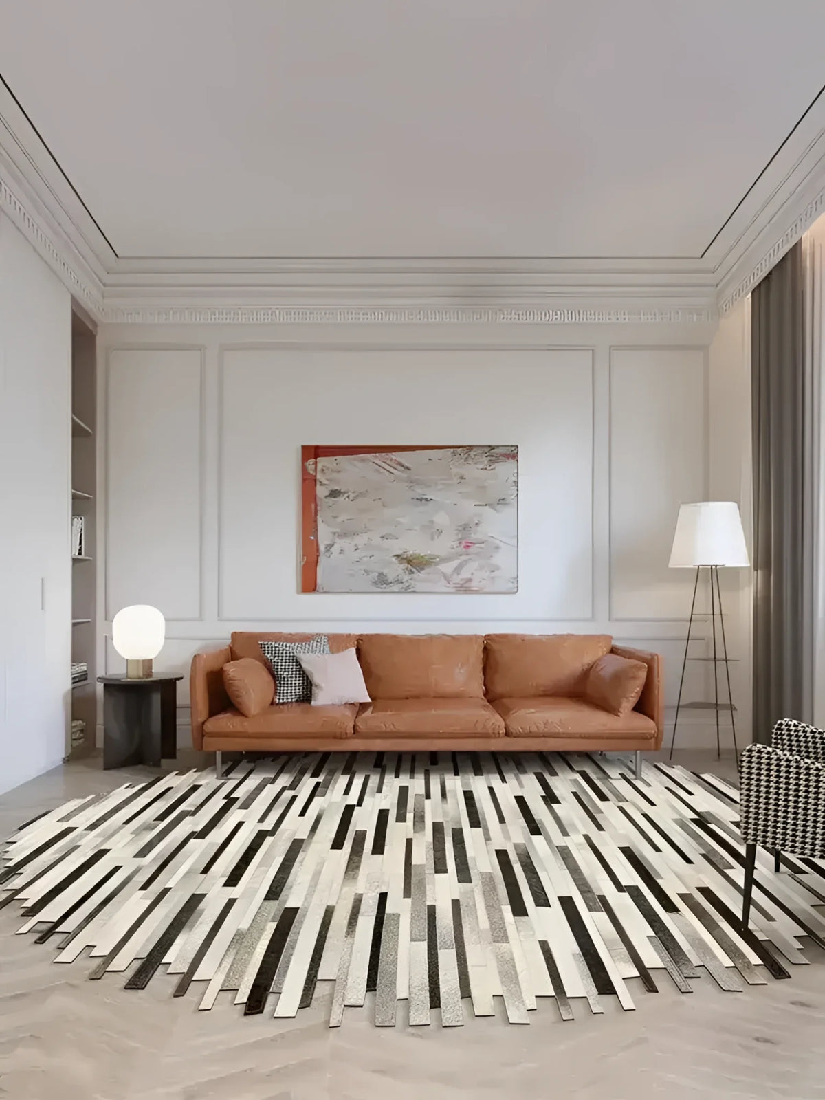 A beautifully styled living room featuring a handmade irregular oval cowhide area rug. The rug, perfect for adding a touch of elegance to any space, is placed under a modern brown leather sofa with throw pillows. This living room setup highlights the rug's unique design, making it an ideal choice for those searching for living room rugs 8x10.