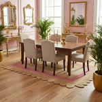 Pink scalloped border jute rug styled in a dining room under walnut table, pink walls, gold ornate mirrors, plants