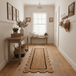 Narrow hallway with wooden floor, rug, table, and wall decorations.