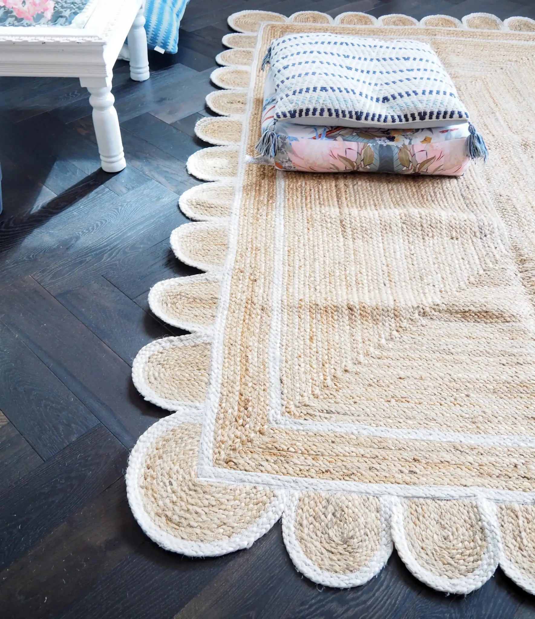 Close-up view of a handmade white scalloped jute rug laid on a dark hardwood floor, perfect for dining room or living room areas. The natural texture and elegant design make it an ideal area rug choice for adding warmth and style to any living space.