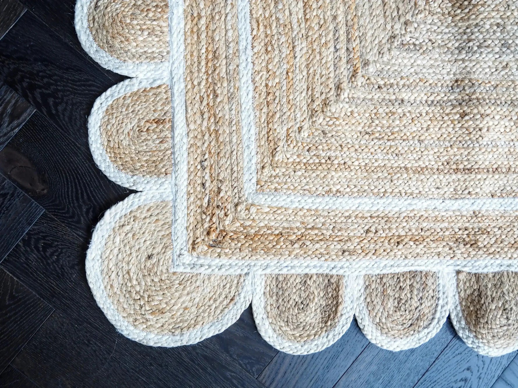 A close-up view of a handmade jute rug with a white scalloped trim, beautifully displayed on dark wooden flooring. This area rug is perfect for adding a natural touch to living room spaces.