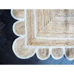 A close-up view of a handmade jute rug with a white scalloped trim, beautifully displayed on dark wooden flooring. This area rug is perfect for adding a natural touch to living room spaces.