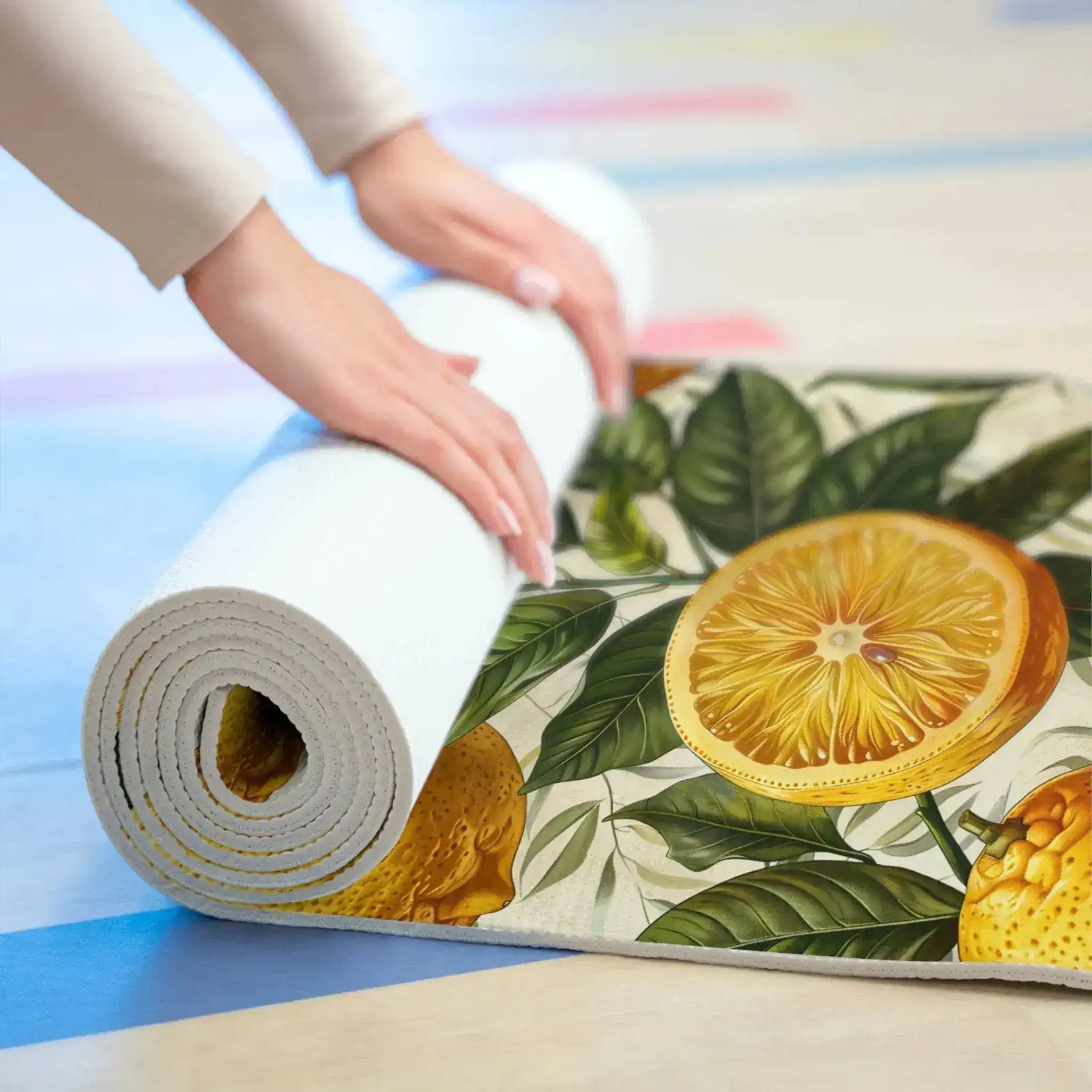 Hands rolling up a lemon-print yoga mat on a studio floor, white cushioned underside coiling inward