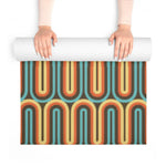 Hands unrolling a yoga mat with retro looping lines in teal, orange and cream on brown