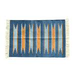 Handwoven Earth and Ocean Cotton Rug with Fringes. This large area rug features a vibrant, boho design with vertical stripes in shades of blue and orange, perfect for under a dining table. The cotton material and fringe detailing add texture, making it a stylish addition to any dining room.