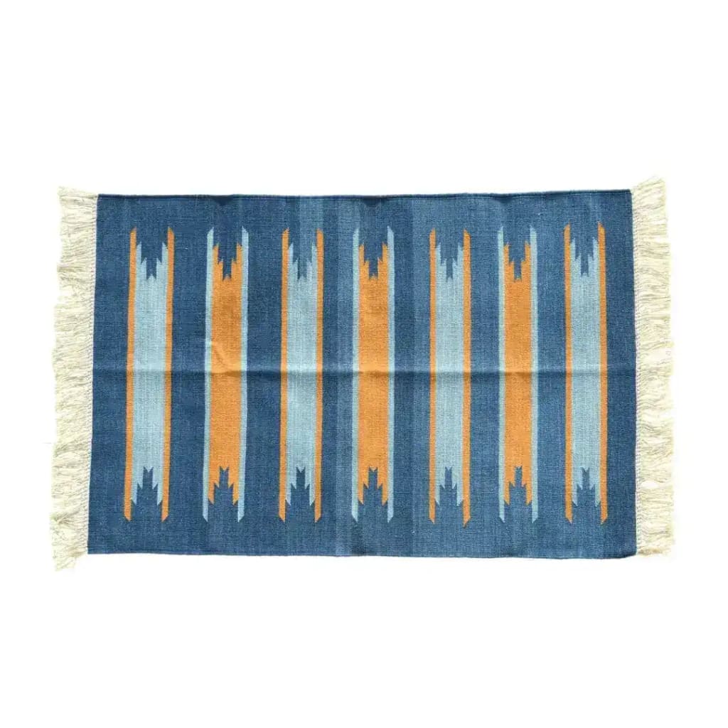 Handwoven Earth and Ocean Cotton Rug with Fringes. This large area rug features a vibrant, boho design with vertical stripes in shades of blue and orange, perfect for under a dining table. The cotton material and fringe detailing add texture, making it a stylish addition to any dining room.
