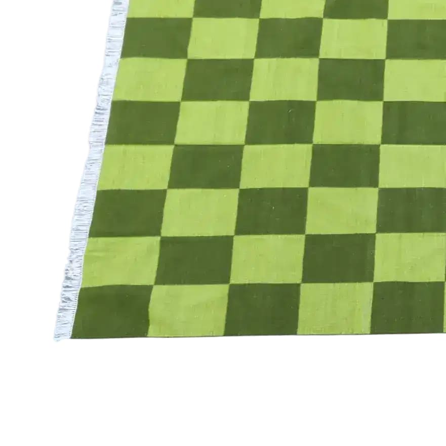 Close-up of a handwoven green checker cotton area rug, perfect for adding a boho touch to your living room or bedroom. This stylish rug features a vibrant green pattern with fringed edges, ideal for those seeking living room area rugs or boho rugs for bedrooms.
