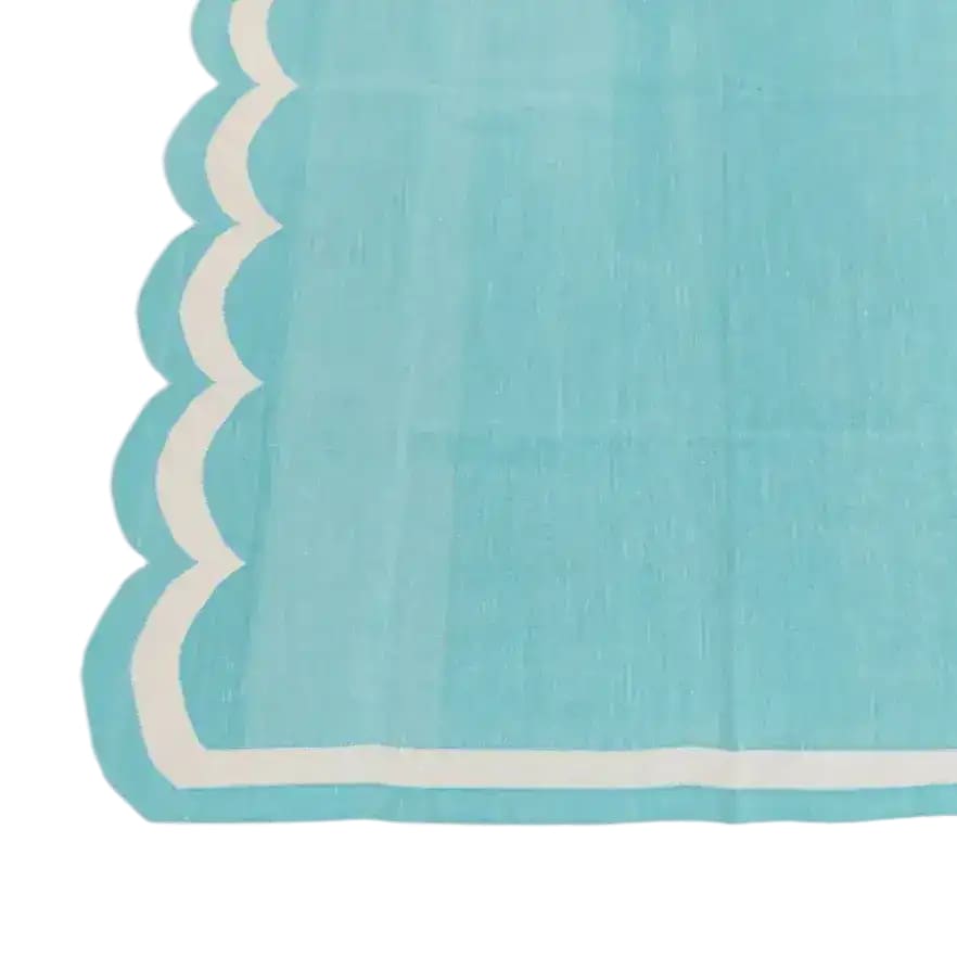 A close-up view of a handwoven reversible cotton scalloped rug in blue, perfect for adding a touch of boho charm to your bedroom or living room. This area rug features intricate scalloped edges and is ideal for use as a living room area rug, measuring 8x10, enhancing your home decor with its vibrant color and unique design.