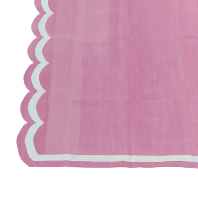 Close-up view of a handwoven reversible pink cotton area rug with scalloped edges, perfect for adding a boho touch to your living room or dining room. This elegant cotton rug is ideal as a dining table rug, enhancing any space with its soft texture and stylish design.