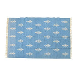 This is a beautifully handwoven white floral blue cotton rug, perfect for adding a touch of boho elegance to your living room. The large area rug features intricate white floral patterns on a soft blue background, complemented by delicate fringes on the edges. Ideal for those looking to enhance their space with a stylish and functional large area rug for living room settings.