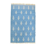 Top view of a handwoven white floral blue cotton area rug with fringes, ideal for large living rooms. This boho rug features a soft blue background adorned with elegant white floral patterns, perfect for adding a touch of style to your living space. Its cotton material ensures durability and comfort, making it a great choice for those seeking large area rugs for their living room.
