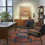 A stylish office space featuring a Heritage Bloom Hand Knotted Area Rug. This vintage rug showcases intricate Persian designs, adding elegance to the large living room setting. The vibrant patterns complement the modern wooden furniture and the framed artwork on the wall, creating a harmonious and inviting atmosphere.