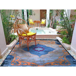 The Heritage Voyage Hand Tufted Rug in an elegant setting, featuring a vibrant vintage pattern with intricate blue and orange designs. Perfect as a centerpiece in a dining room or living room, this 8x10 wool area rug adds a touch of classic charm, surrounded by natural decor and wooden furniture.