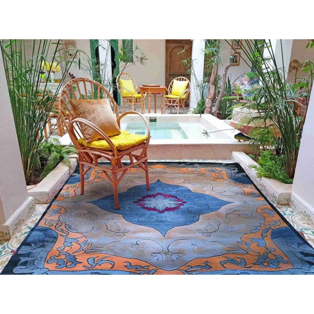 The Heritage Voyage Hand Tufted Rug in an elegant setting, featuring a vibrant vintage pattern with intricate blue and orange designs. Perfect as a centerpiece in a dining room or living room, this 8x10 wool area rug adds a touch of classic charm, surrounded by natural decor and wooden furniture.