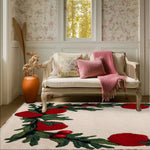 A cozy living space featuring the Holly Berry Bliss Hand Tufted Area Rug, perfect for an office or dining room. This wool rug showcases vibrant red holly berries and lush green leaves on a soft, cream background, adding warmth and elegance to the room. The setting includes a comfortable loveseat with pink cushions and a throw, complemented by a terracotta vase and floral wallpaper, enhancing the inviting atmosphere.