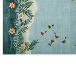 A vibrant area rug featuring a serene design with green leaves and orange flowers along the left border, complemented by colorful hummingbirds across a blue background. Perfect for enhancing the elegance of any living room, this wool rug offers style and comfort, making it an ideal choice for large living room rugs.