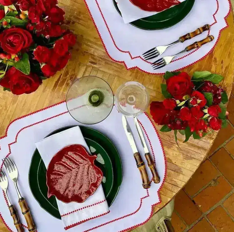 Imperial Crimson Placemats two-place setting — white mats with crimson bead-dot border, green plates and red floral centerpiece