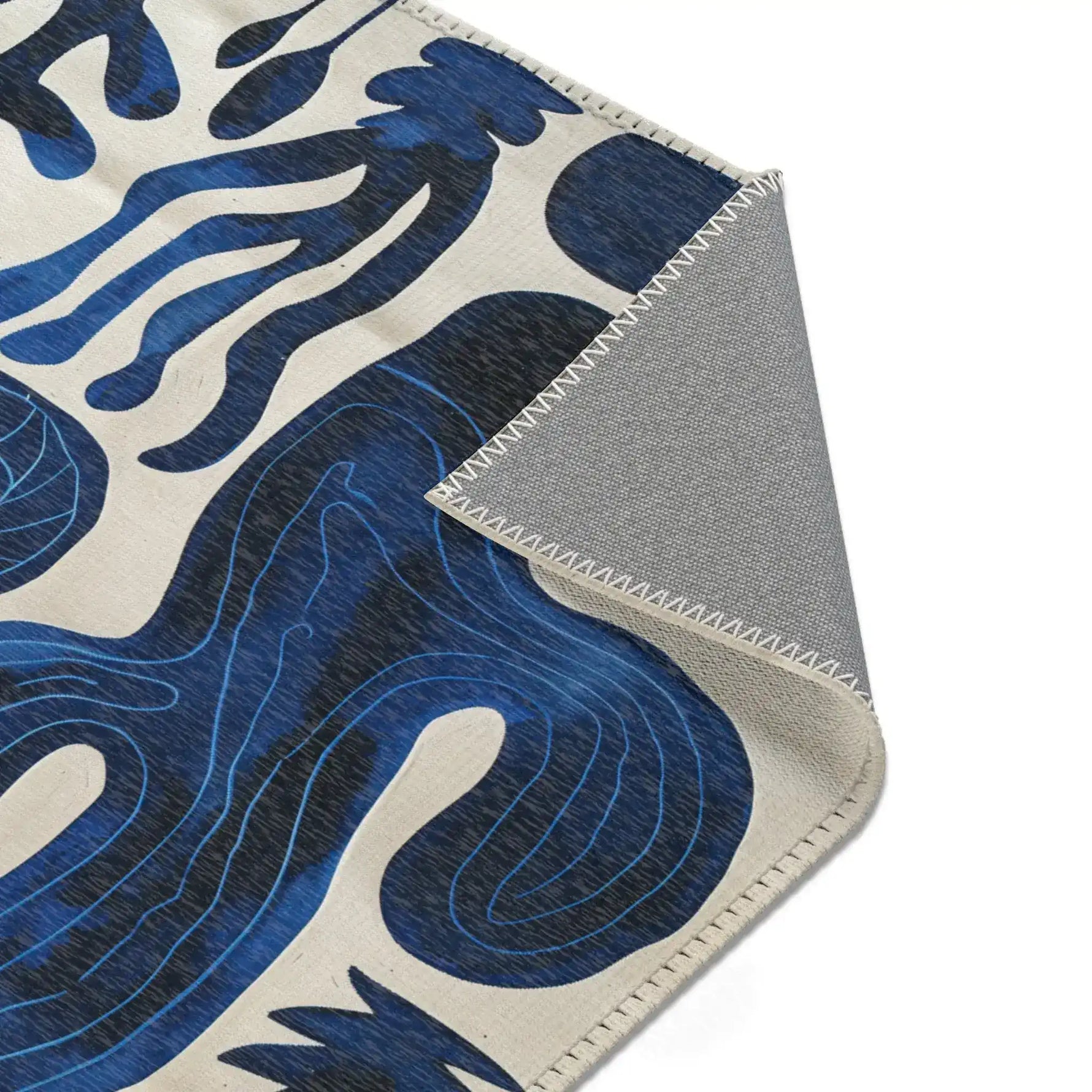 Indigo Desert Dreams rug corner folded showing grey non-slip backing with blue abstract botanical pattern on cream face