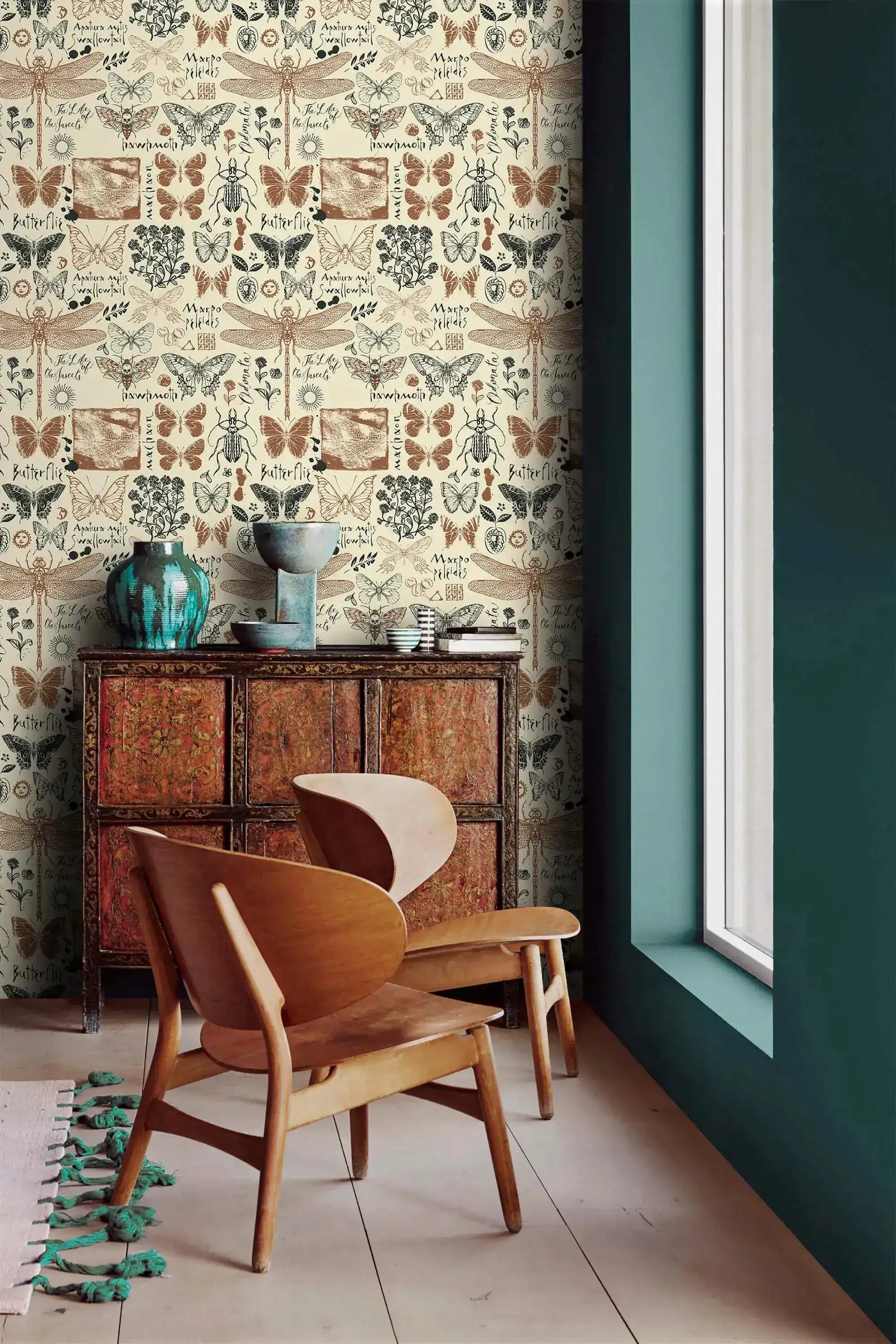 Insect garden wallpaper in cream with butterflies and beetles beside a teal wall and carved wood cabinet