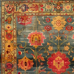 A detailed view of an intricate bloom wool hand-knotted area rug, featuring vibrant floral patterns in shades of red, yellow, and orange set against a muted blue background. This square area rug showcases a vintage Persian style, perfect for adding a touch of elegance to a bedroom or living room.