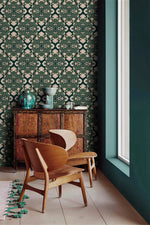 Intricate floral block print wallpaper by a window, cream blooms on teal above a carved wood cabinet
