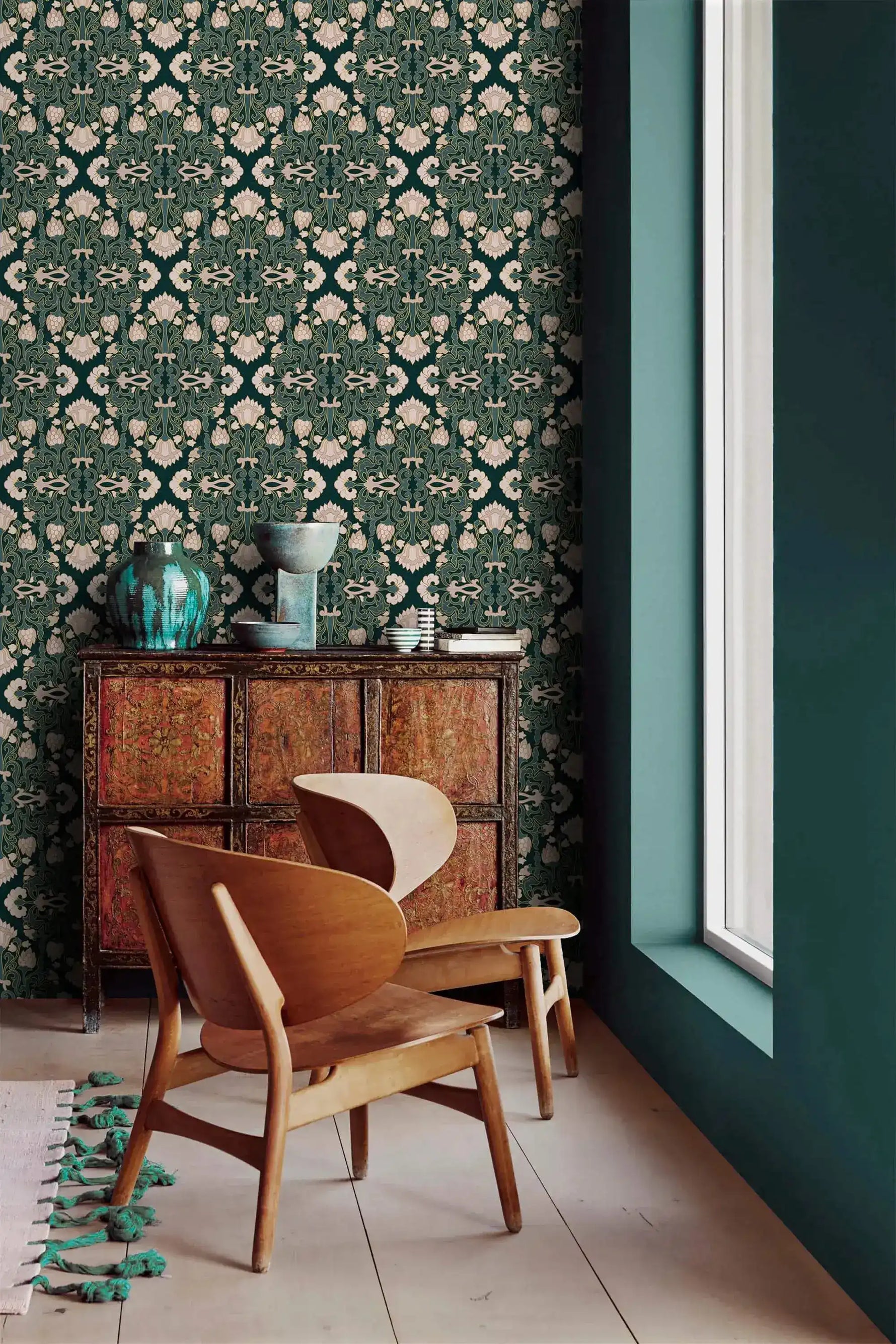 Intricate floral block print wallpaper by a window, cream blooms on teal above a carved wood cabinet