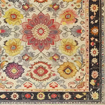 Close-up of an intricately designed hand-tufted area rug featuring vibrant floral patterns in red, yellow, and purple hues, ideal for adding a vintage touch to living room spaces. This wool rug showcases a detailed border and is perfect for those seeking unique living room area rugs with a floral theme.