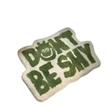 A whimsical area rug with the phrase 'Don't Be Shy' in bold green letters, perfect for adding a playful touch to living room area rugs. This irregularly shaped rug features a unique design that stands out in any space, making it an ideal choice for area rugs for living room decor.