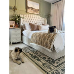 A cozy bedroom features a stylish area rug with a vintage design, perfect for large living rooms. The wool rug adds elegance and warmth, complemented by a plush bed and decorative pillows. Two adorable pugs relax in the serene setting, enhancing the inviting ambiance.
