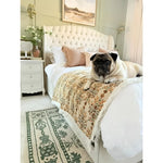 A cozy bedroom featuring a luxurious bed with a plush headboard and a pug comfortably resting on it. Below, an elegant wool area rug with vintage floral patterns adds warmth and style to the space, ideal as a large living room rug or for use in a bedroom setting.