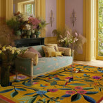A vibrant area rug featuring a bold floral design in a living room setting. The Joyful Jamboree Hand Tufted Rug is crafted from wool, showcasing large colorful flowers and leafy branches on a sunny yellow background. This wool rug complements the elegant living room decor with its luxurious and artistic touch, ideal for large living room spaces.